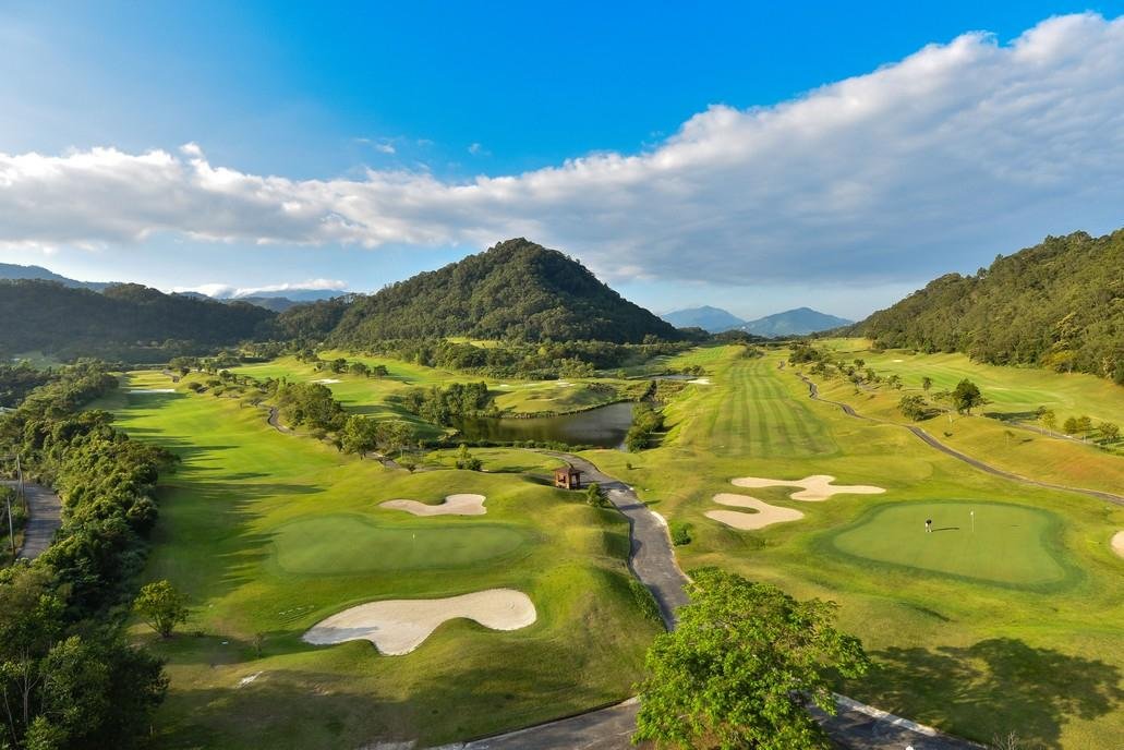 Aerial view of Sunshine Valley golf course: greens, bunkers and a pond in a wooded valley